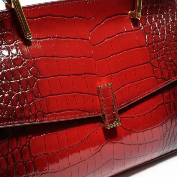 Close-up of red crocodile leather satchel bag with gold rectangular clasp and handle detailing