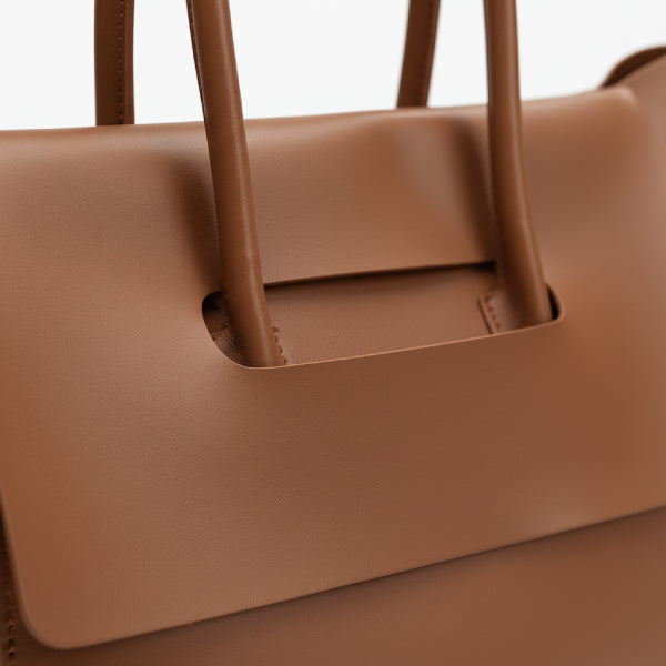 Close-up of the handle of the Sylvene vegan leather tote bag in caramel color, emphasizing its smooth texture and sophisticated design