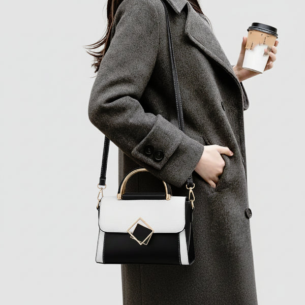 Model in a grey coat holding a black and white vegan leather satchel bag with a geometric design, perfect for a sophisticated and modern outfit