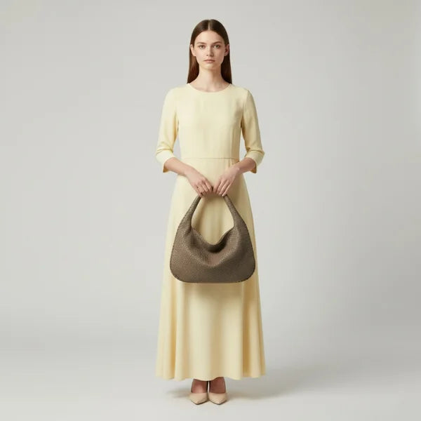 Model standing with grey woven vegan leather hobo bag, wearing a yellow dress, showcasing the bag's elegant design