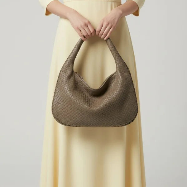 Model holding grey woven vegan leather hobo bag with braided handle, zipper closure, and spacious design