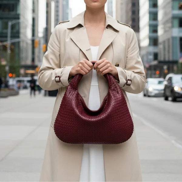 Model holding wine red woven vegan leather hobo bag with braided handle, zipper closure, and spacious design in an urban setting