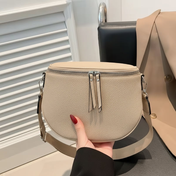 Handheld view of an apricot vegan leather crossbody bag featuring a round design with zipper detail and adjustable shoulder strap