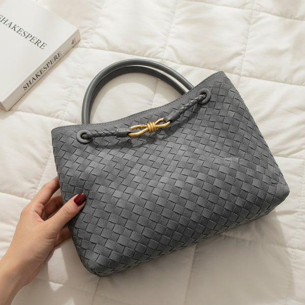 Close-up of the Veyra vegan leather tote bag in gray, held by a hand, showcasing its elegant woven texture and gold-tone knot closure