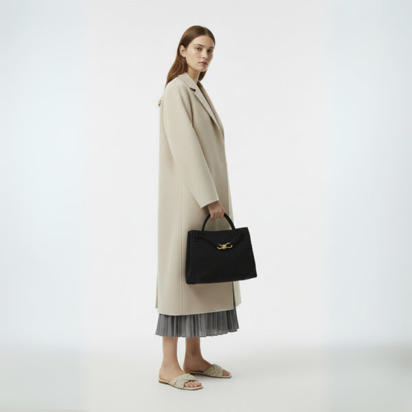 Model carrying the Veyra vegan leather tote bag in black, styled with a beige coat and pleated skirt, exuding an elegant and modern look