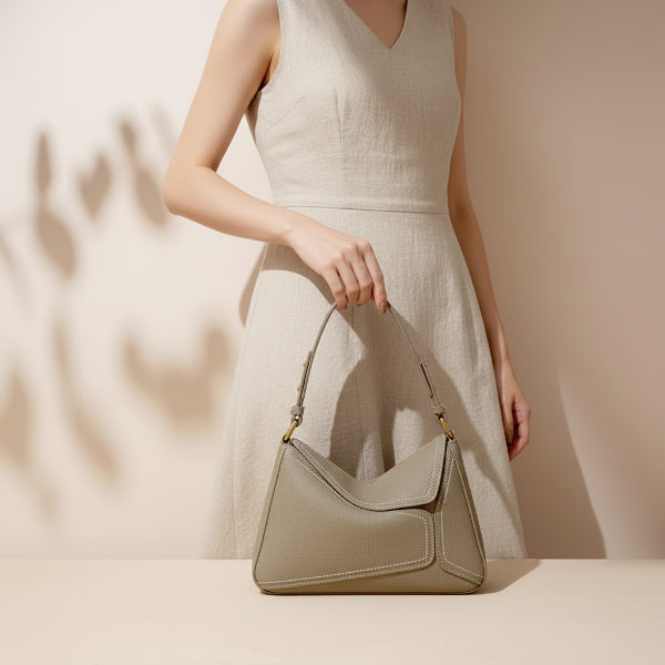 Model holding Virella beige leather hobo bag with gold accents, paired with a light dress for a stylish look
