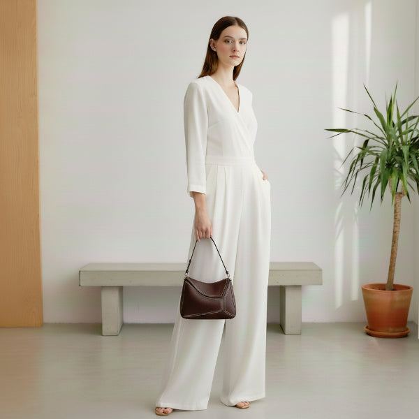 Model holding Virella coffee brown leather hobo bag while wearing a white jumpsuit, styled with minimalist elegance