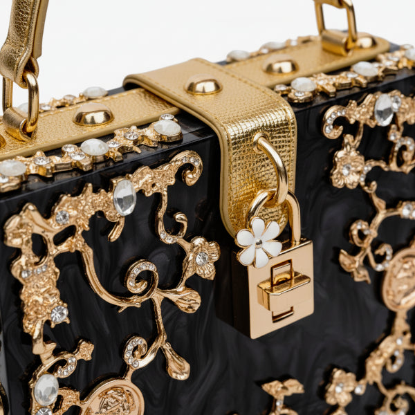 Close-up of Zephyra acrylic evening bag in black with detailed floral gold embellishments and lock clasp