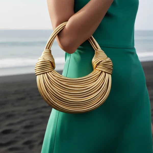 Zyra Vegan Leather Evening Bag in gold, lifestyle seaside shot with model showing arm carry and statement crescent shape
